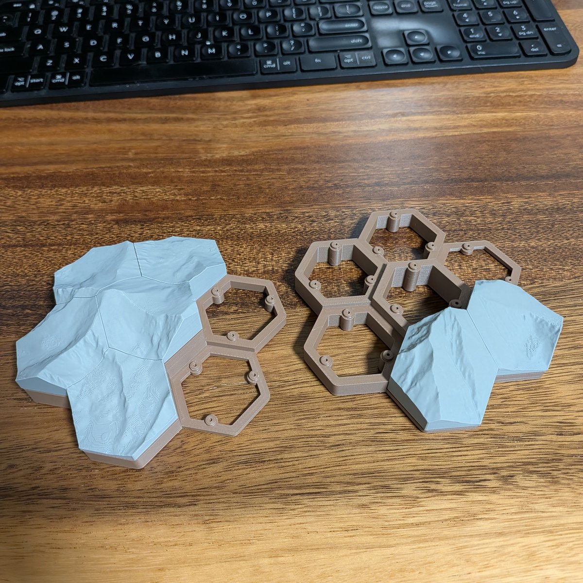 Gray topographic hex tiles partly lifted out of a tan hexagonal pedestal on a wooden desk
